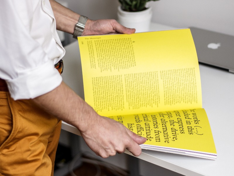 A Man Surveying a Yellow Magazine on Desk