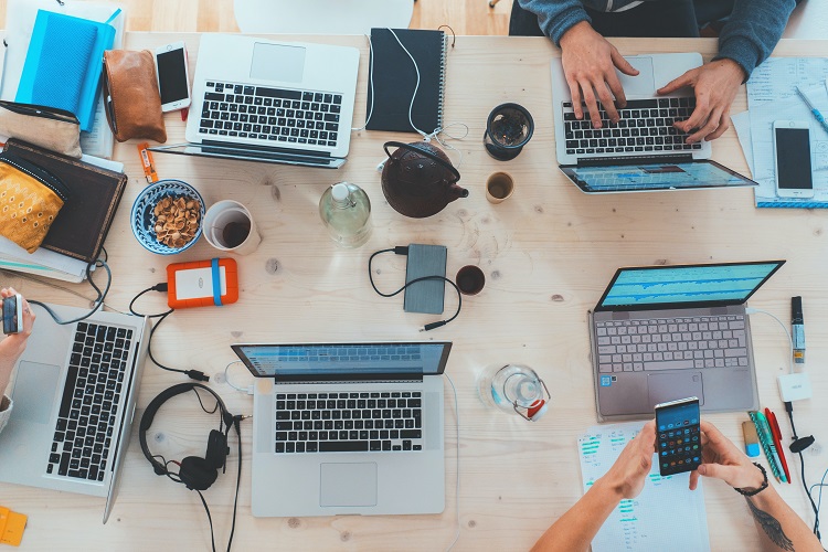 A Crowded Desk with Laptops, NoteBooks and Snacks